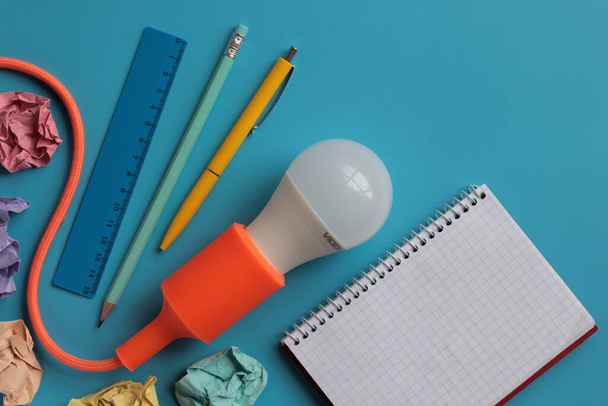 Kreatív elrendezés villanykörte, jegyzettömb, toll, ceruza, vonalzó és gyűrött papír kék alapon. Kreatív ötlet koncepció üzleti, projekt vagy ötletbörze számára. - Fotó, kép