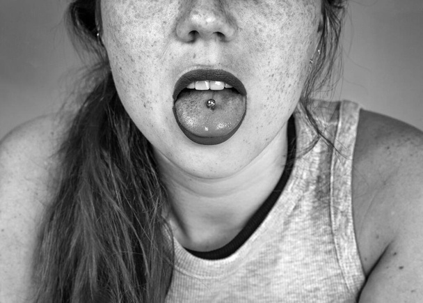 Ritratto ravvicinato di giovane donna che sporge la lingua trafitta, mostrando la sua lingua piercing in bianco e nero - Foto, immagini