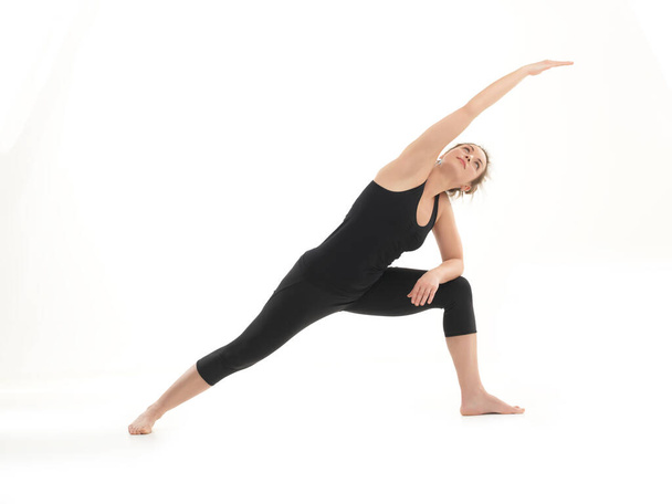 vista de cuerpo completo de la joven mujer delgada en postura de yoga, vestida de negro en tocino blanco - Foto, Imagen