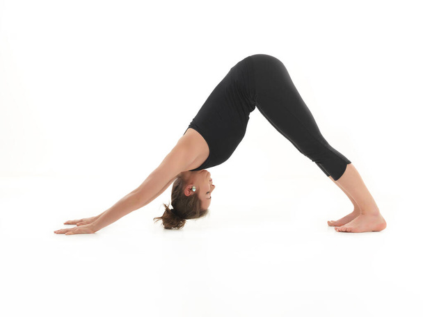 young woman sitting in stretching yoga pose, dressed in black, on white background - Photo, Image