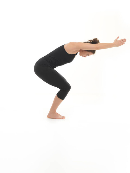 side view of attractive young woman demonstrating yoga pose, dressed in black, on white background - Photo, Image