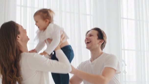 Jeunes parents soucieux heureux mère et père, maman et papa caucasiens ascenseur jeter petite fille bébé dans l'air attraper enfant tout-petit bébé fille rire jouer jeu avec enfant à la maison, week-end en famille à l'intérieur - Séquence, vidéo