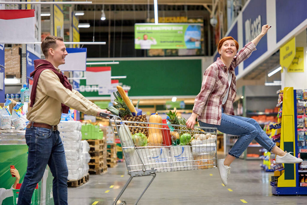 Running and laughing. couple goofing around together, laughing and running while riding shopping cart. - Zdjęcie, obraz