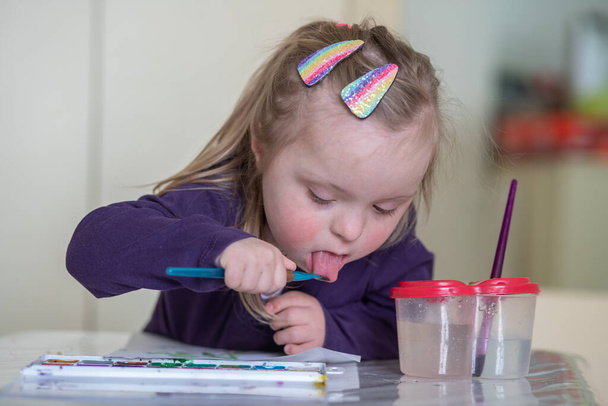  girl with Down syndrome paints with watercolors. - Photo, Image
