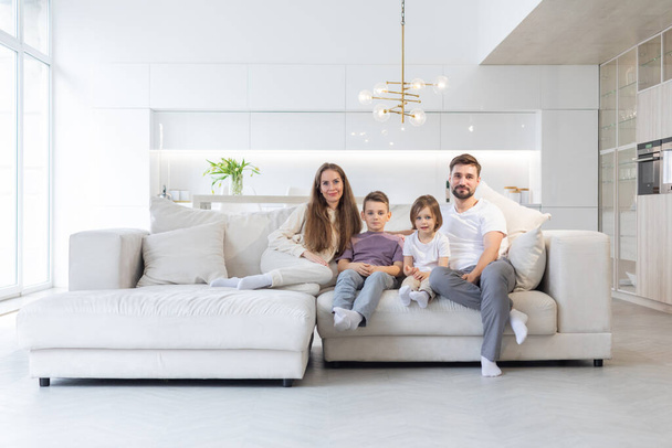 Family portrait of young parents with their two children at home, white modern desgin of living room - Photo, image