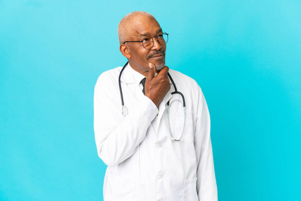 Senior arts man geïsoleerd op blauwe achtergrond en op zoek omhoog - Foto, afbeelding