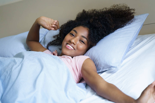 Αφρο-αμερικανική γυναίκα που τεντώνεται στο κρεβάτι το πρωί - Φωτογραφία, εικόνα