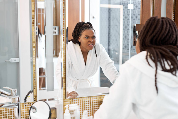 Jeune femme noire regardant anxieusement reflet miroir dans la salle de bain - Photo, image