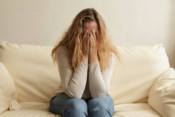 Внутрішній образ сумної і напруженої молодої жінки, що прикриває обличчя руками і плаче вдома
. - Фото, зображення