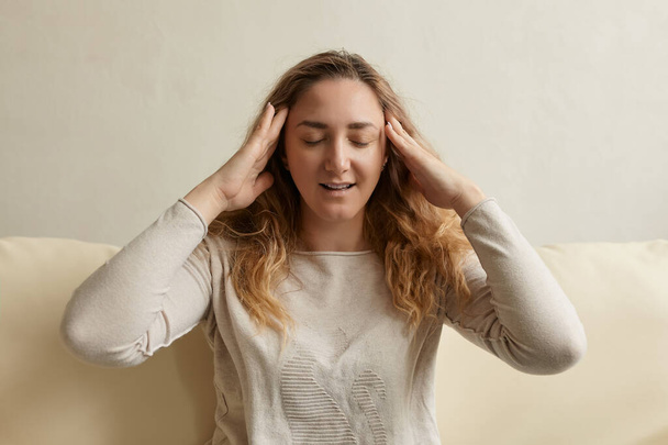 Mujer estresada calmándose aliviando el dolor de cabeza alivio del estrés emocional, mujer joven nerviosa meditando masajes en las sienes haciendo ejercicios de respiración en el sofá interior - Foto, Imagen