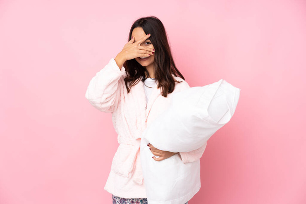 Young woman in pajamas isolated on pink background covering eyes by hands and smiling - Photo, Image