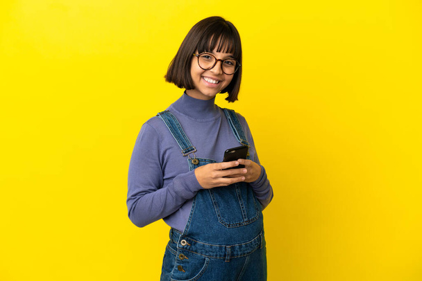 Junge schwangere Frau über isoliertem gelben Hintergrund sendet eine Nachricht mit dem Handy - Foto, Bild