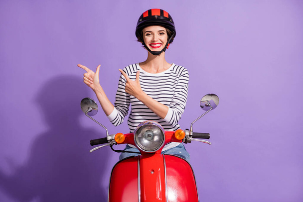 Photo of cheerful girl drive retro moped direct fingers empty space wear helmet striped shirt isolated violet color background - Fotoğraf, Görsel