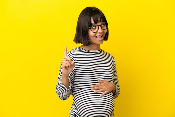 Mujer embarazada joven sobre fondo amarillo aislado con la intención de darse cuenta de la solución mientras levanta un dedo - Foto, Imagen