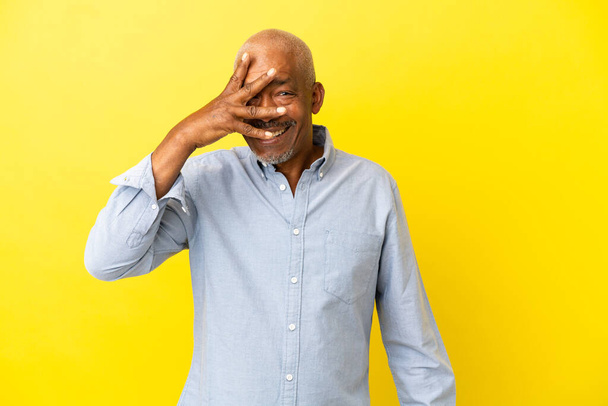 Cuban Senior isolated on yellow background covering eyes by hands and smiling - Φωτογραφία, εικόνα