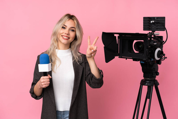 Toimittaja nainen jolla on mikrofoni ja raportointi uutisia yli eristetty vaaleanpunainen tausta osoittaa voiton merkki molemmin käsin - Valokuva, kuva