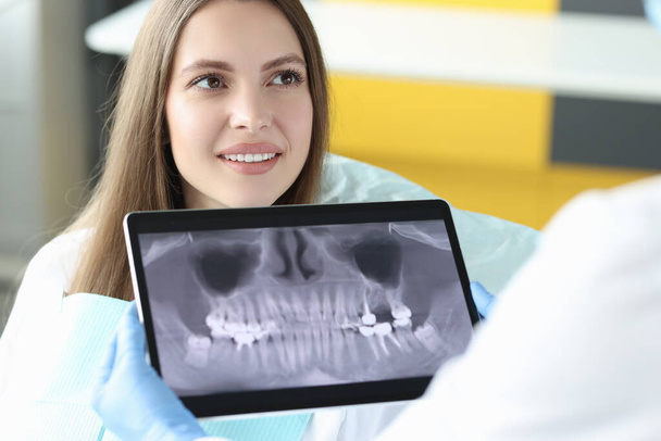 Portrait de femme souriante au rendez-vous chez le dentiste tenant un comprimé avec une image radiographique de la mâchoire - Photo, image