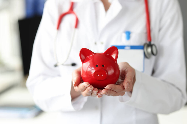Doctor holds red pig piggy bank in his hands - Photo, Image