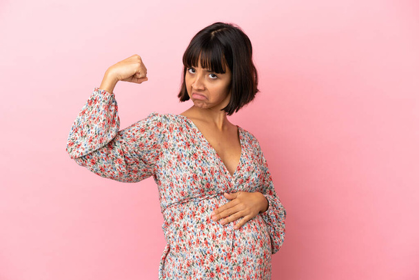 Молодая беременная женщина на изолированном розовом фоне делает сильный жест - Фото, изображение