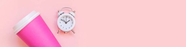 Simply flat lay design pink paper coffee cup and alarm clock isolated on pink pastel background. Takeaway drink breakfast beverage. Good morning wake up awake concept. Top view copy space banner - Photo, Image