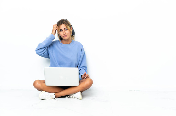 Jovem loira uruguaia com o laptop isolado no fundo branco com dúvidas e com expressão facial confusa - Foto, Imagem