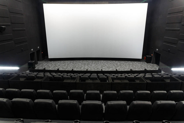 Empty cinema auditorium with line of black chairs, stage and projection screen. Ready for adding your own picture. - Фото, изображение
