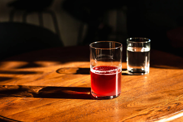 A sweet and sour refreshing blackberry gin bramble cocktail in a highball glass without ice in direct hard sunlight with long shadows, on a wooden table, horizontal photo with copy space - Photo, Image