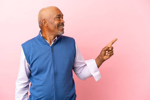 Кубинский старший изолирован на розовом фоне, указывая пальцем в сторону и представляя продукт - Фото, изображение