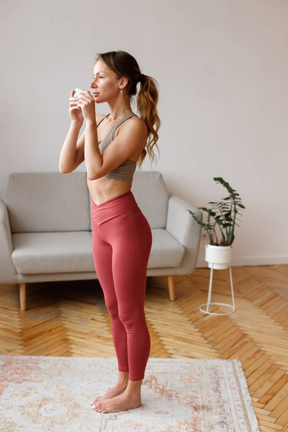 Sportos nő leggings iszik vizet a nappaliban - Fotó, kép