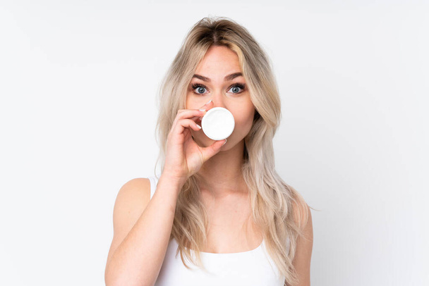 Teenager blonde girl over isolated white background with moisturizer - Photo, image