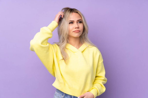 Teenager girl wearing a yellow sweatshirt over isolated purple background having doubts and with confuse face expression - 写真・画像