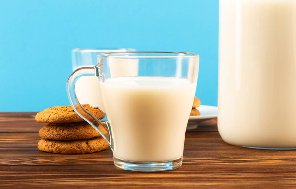 A jug and a glass of milk on a wooden table, on a blue background. - Foto, afbeelding