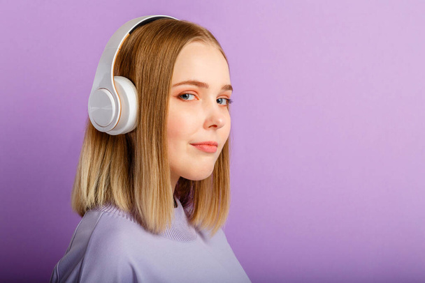 Confident Young woman in headphones portrait. Beautiful serious woman with blonde hairstyle enjoy listen song music in headphone isolated over purple color background. Copy space - Valokuva, kuva