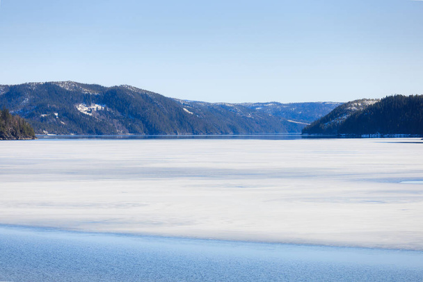 Kevätmaiseman sulaminen. Metsäjärvi osittain jään peitossa ja osittain heijasteli sinistä taivasta ja vuoria kevätpäivän alussa.. - Valokuva, kuva