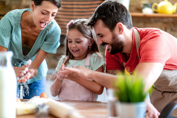 Vater, Mutter und Tochter spielen mit Teig, während sie zu Hause in der Küche Teig backen. - Foto, Bild
