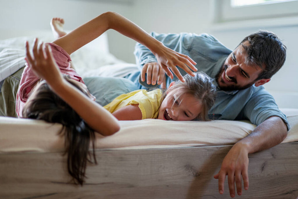 Lächelnde junge Familie genießt in ihrem Schlafzimmer.Sie verbringen ihre Freizeit zu Hause und haben Spaß. - Foto, Bild