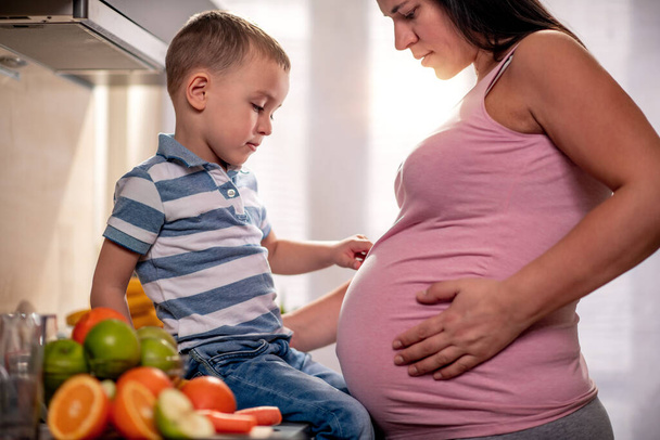 Mujer embarazada con su hijo jugando juntos en la cocina.  - Foto, imagen