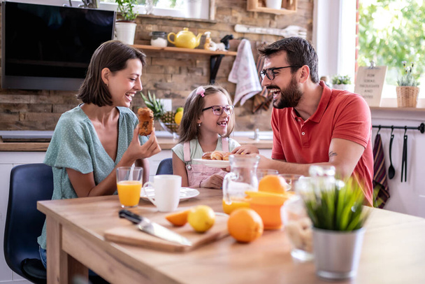 Семья, еда и счастье: счастливые мать, отец и дочь завтракают дома. - Фото, изображение