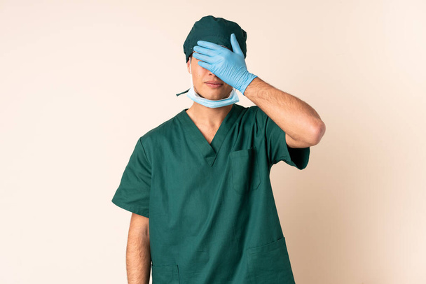 Surgeon man in blue uniform over isolated background covering eyes by hands - Valokuva, kuva