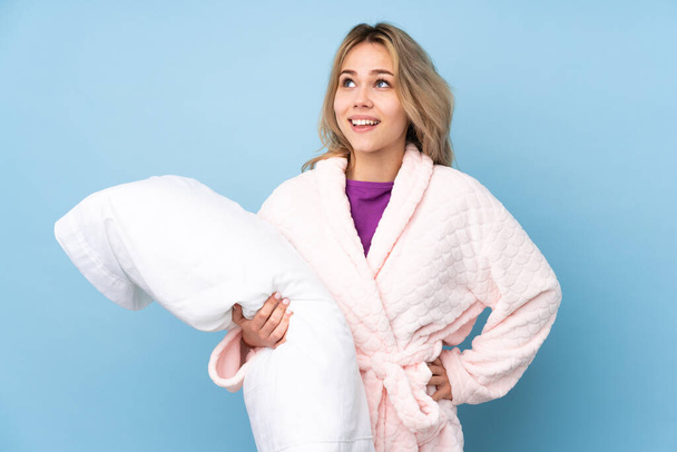 Teenager Russian girl in pajamas isolated on blue background posing with arms at hip and smiling - Photo, Image