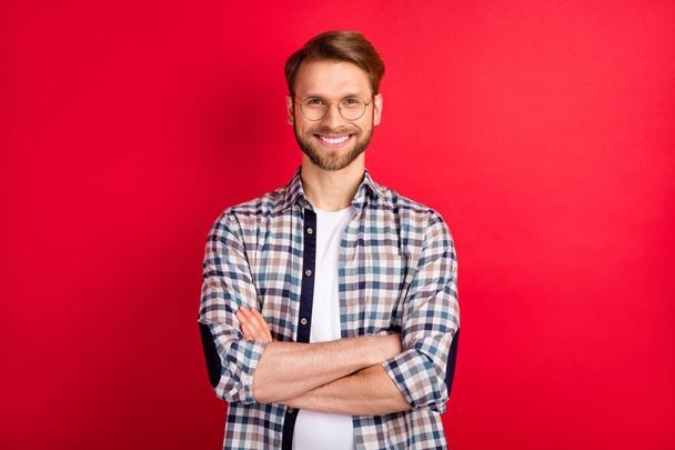 Fénykép elég magabiztos fiatal úriember öltözött kockás ing szemüveg kéz hajtogatott mosolygós elszigetelt piros szín háttér - Fotó, kép