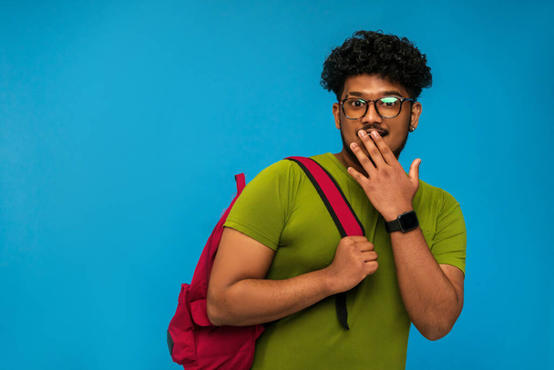Indian student isolated on blue background with backpack surprised and smiling looking at camera, place for text. - Valokuva, kuva
