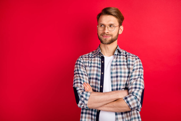 Photo of serious pretty gentleman dressed plaid shirt spectacles hands folded looking empty space isolated red color background - Zdjęcie, obraz