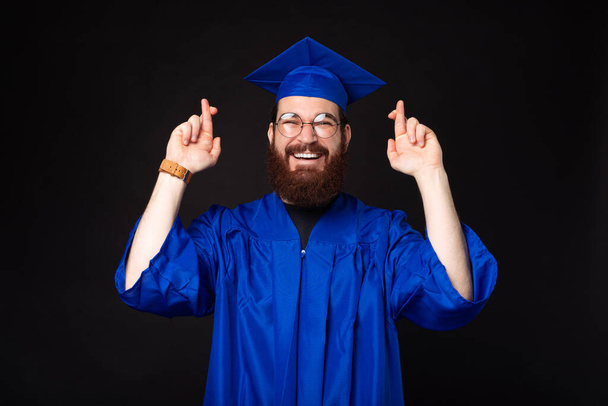 Φωτογραφία του χαρούμενου γενειοφόρου άνδρα σε μπλε bachelor σταυρώνουν τα δάχτυλα και επιθυμούν. - Φωτογραφία, εικόνα