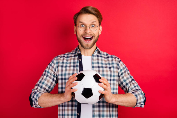 Photo of impressed funny young gentleman dressed plaid shirt spectacles smiling catching ball open mouth isolated red color background - 写真・画像