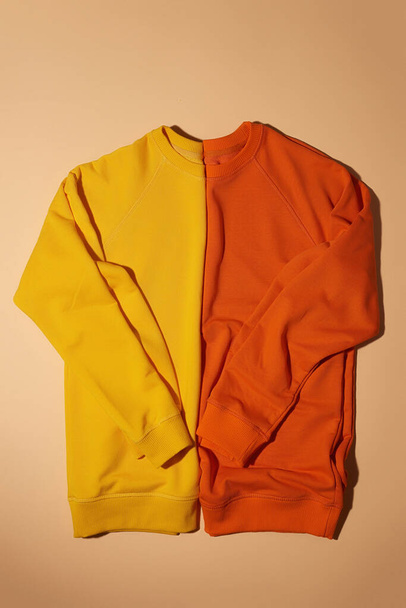 Widok z góry dwóch składanych żółtych i pomarańczowych bluz sportowych leżących pionowo izolowane na jasnym beżowym tle - Zdjęcie, obraz