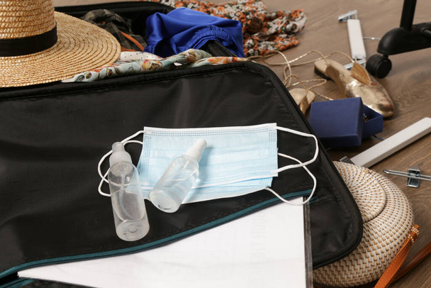 Preparing suitcase for travel during Coronavirus pandemic. Face masks and hand sanitizer with summer clothing in luggage. Travel in new normal concept. - Фото, изображение