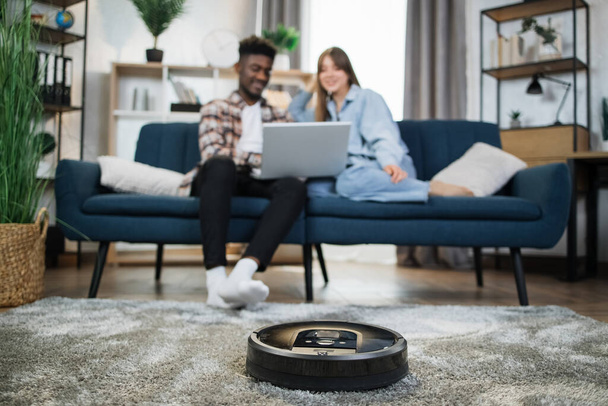 Robot cleaning apartment while couple relaxing on couch - Foto, Bild