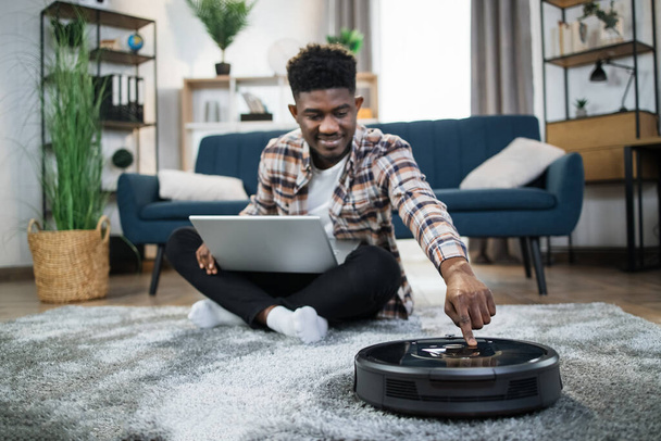 Smiling african man turning on robot vacuum cleaner - Foto, immagini