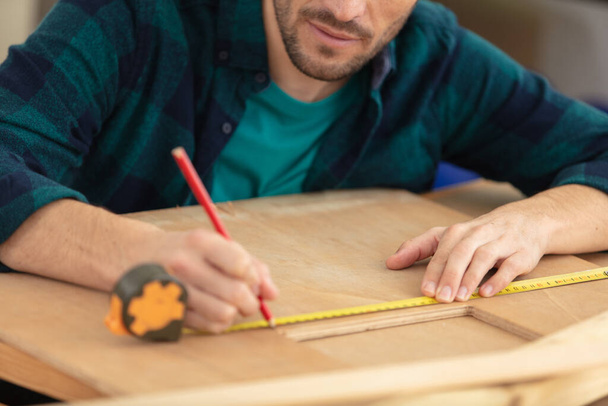 close-up of craftsman hands measuring wooden plank - Foto, afbeelding